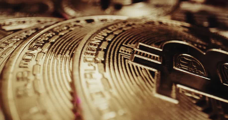 Gold coins with bitcoin symbol sit on maroon surface