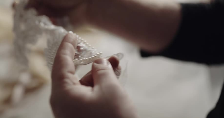 Woman cuts pearl decorated lace fabric with small metal golden scissors