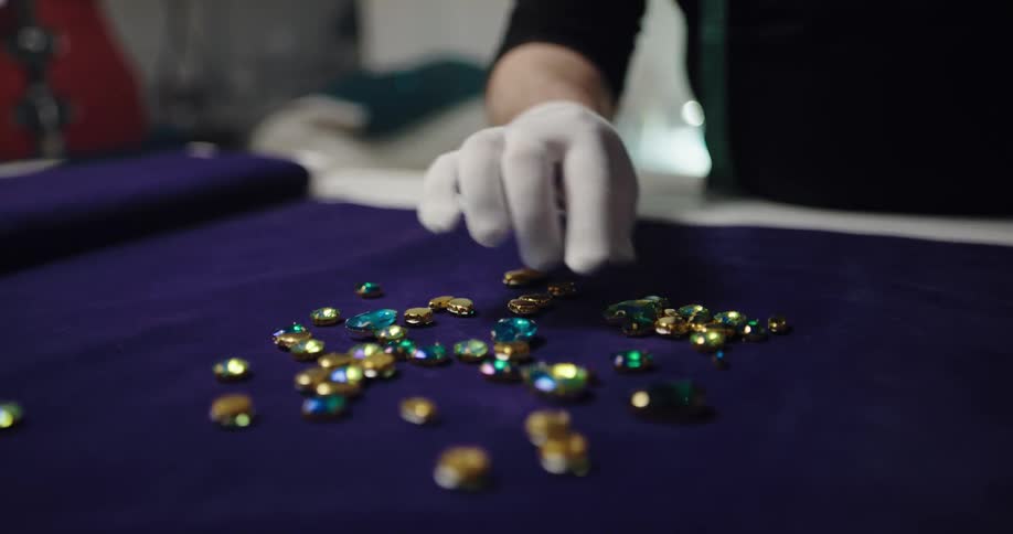 Jeweler wearing a white glove selecting and turning precious stones over a blue cloth