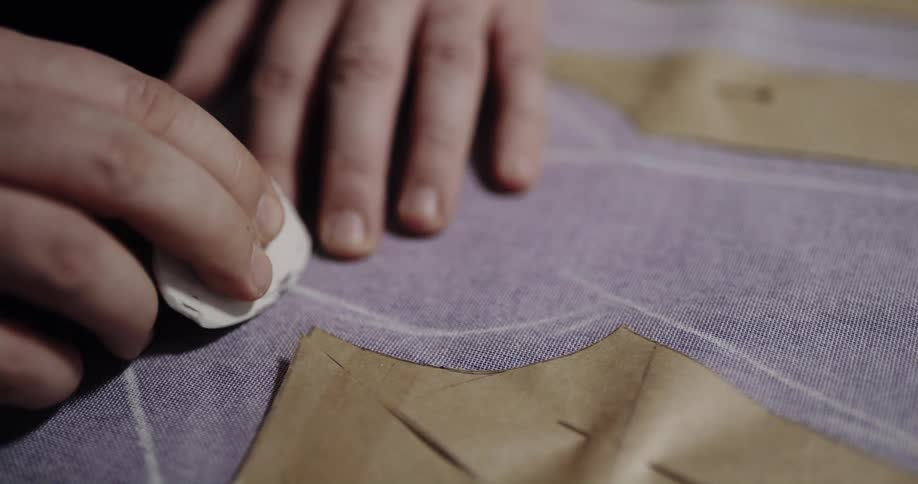 Close up of a fashion designer uses chalk to draw patterns over a piece of cloth