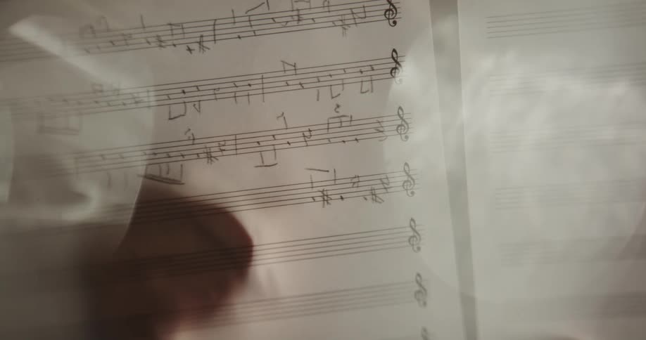 Silhouette of a hand writing musical notes on a music sheet using a pencil