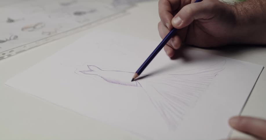 An artist is working on a sketch and other sketches lay across the table