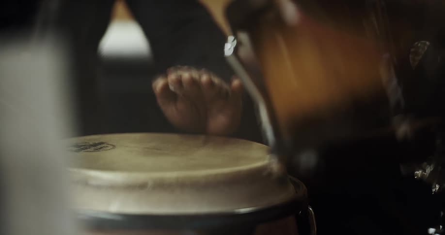 A man plays the bongos in a room full of instruments