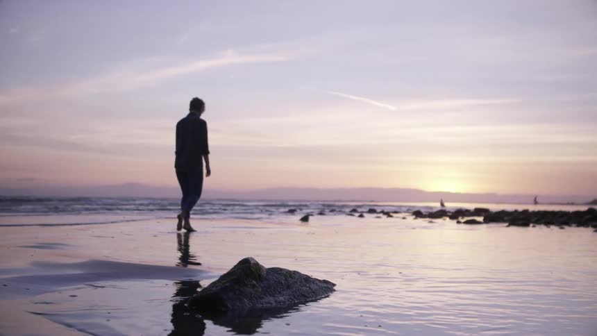 Woman walks on a beach at sunset