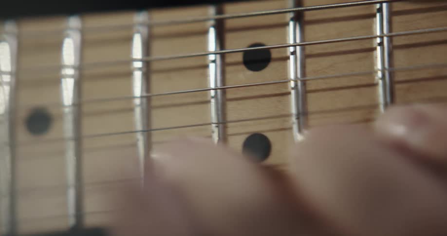 A musician is moving their fingers across the strings and frets as they play a guitar