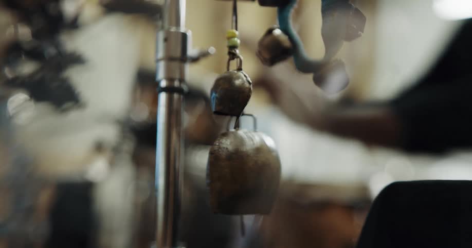 A person strikes a pair of hanging chimes before playing some beats on drums in the background