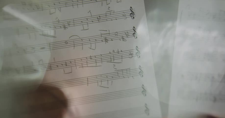 Silhouette of a hand writing musical notes on a music sheet using a pencil