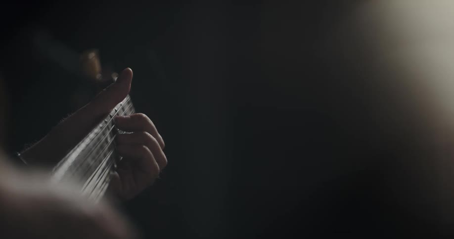 A musician is moving their fingers across the strings and frets as they play a guitar
