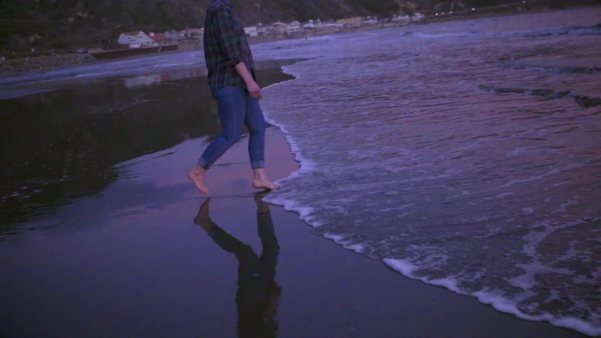 A woman backs away from the water on the beach