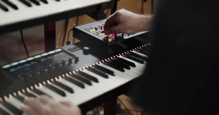 Musician turning the led lit knobs on a mixer over a musical keyboard inside a studio