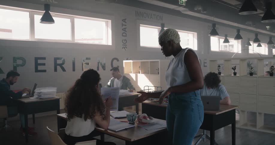 Woman stands near coworkers deskdiscussing documents