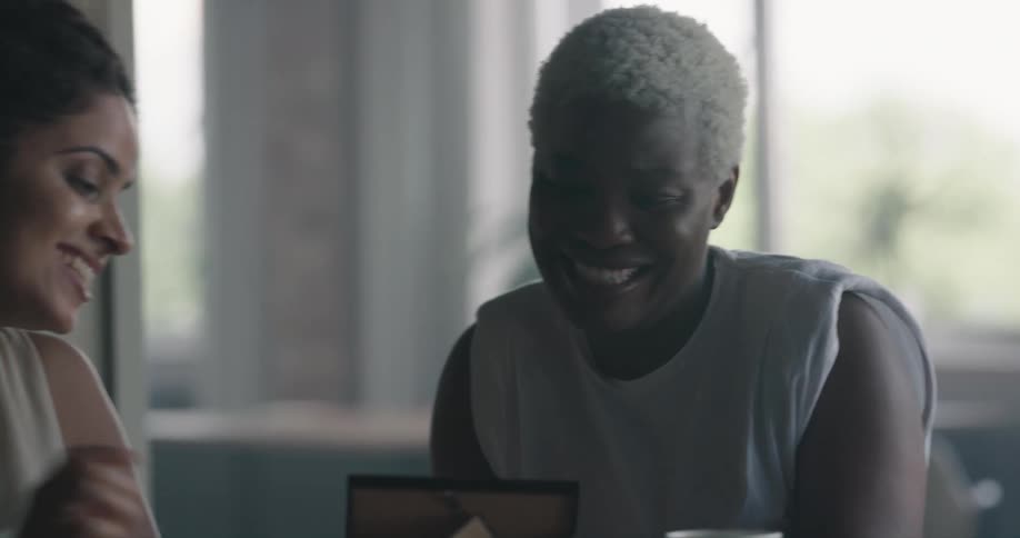 A woman shows a frame photo to a friend who stops drinking coffee to look