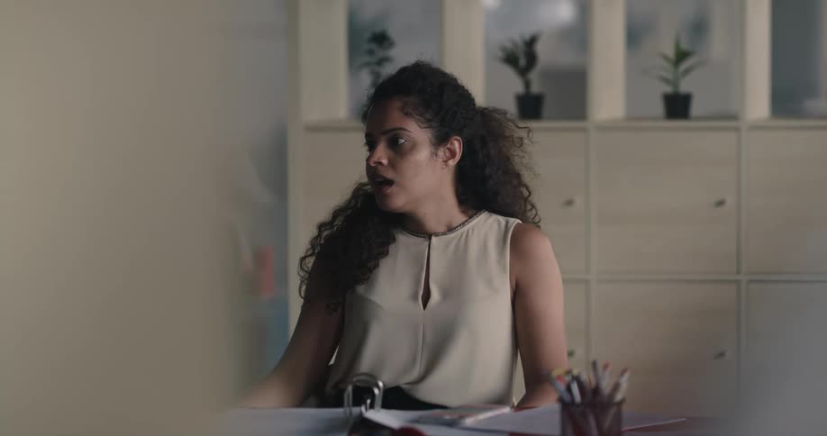 Woman sitting on a chair at a desk in the office talking to a coworker