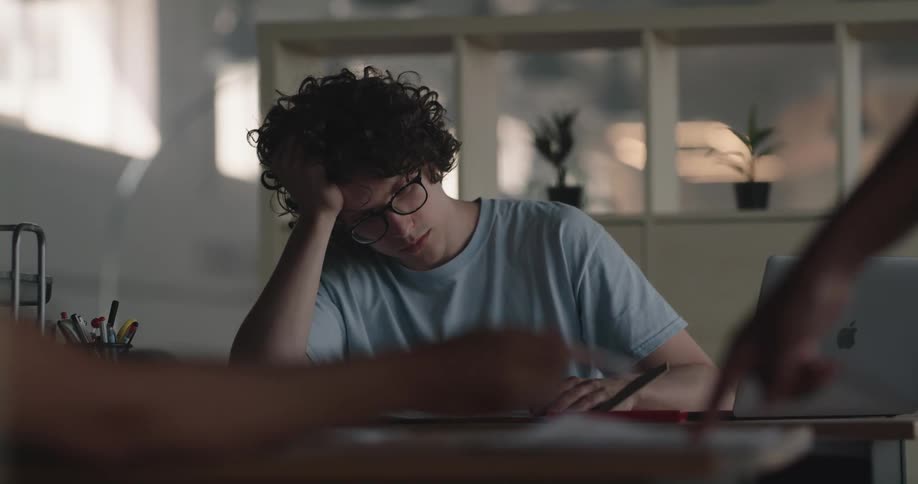 Young bored man sitting at a desk in the office tiredly reading a document