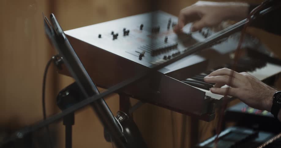A person playing an electric keyboard uses their other hand to adjust various sliders on the instrument