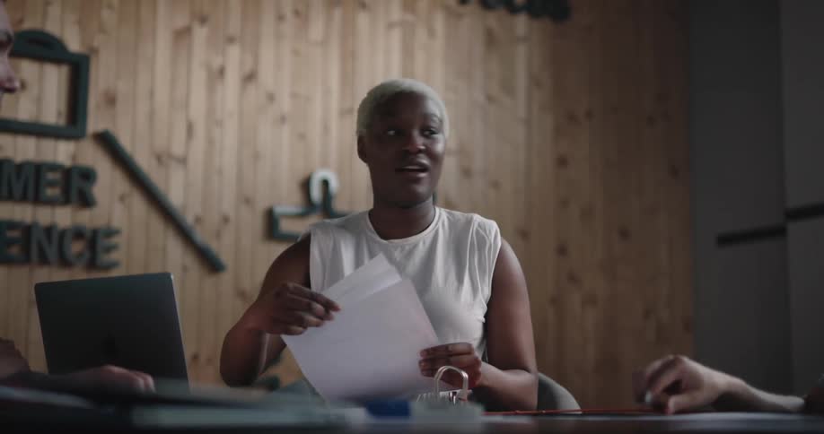 Woman holding a meeting in an office space handing out papers to the coworkers and using her laptop