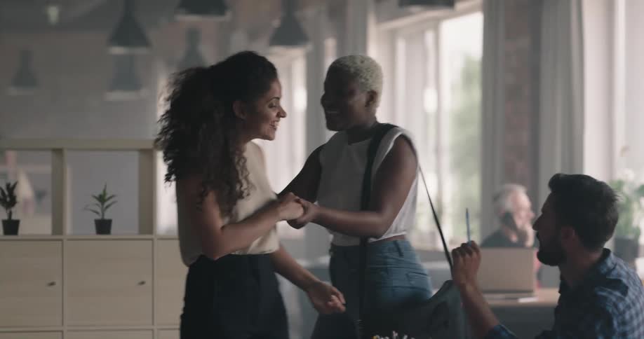 A woman approaches a group of people sitting at a table in an office and greets each of them with a hug