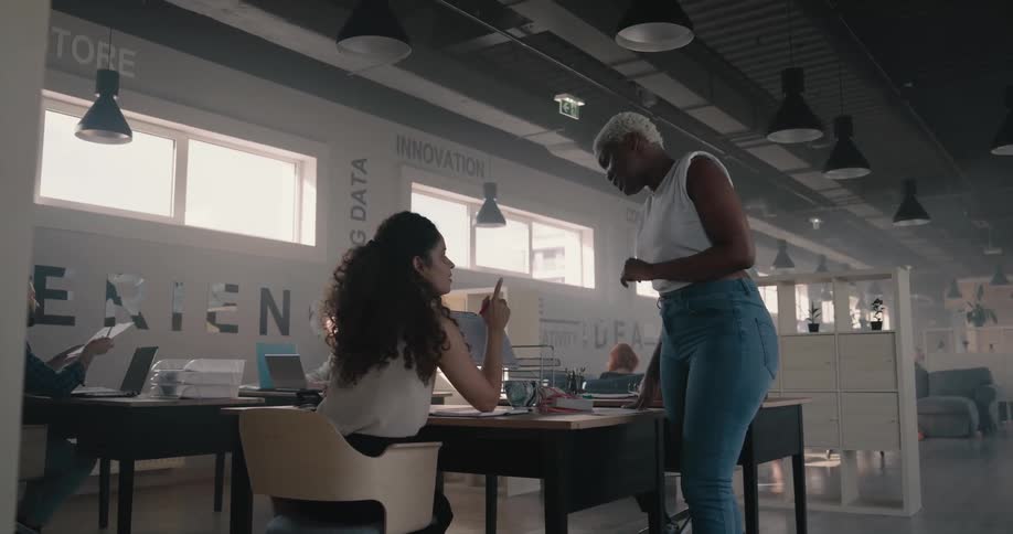 Woman walks through office and stops to discuss document with one worker