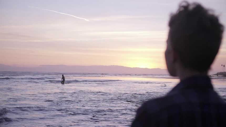 A woman watching a surfer as he heads out to sea