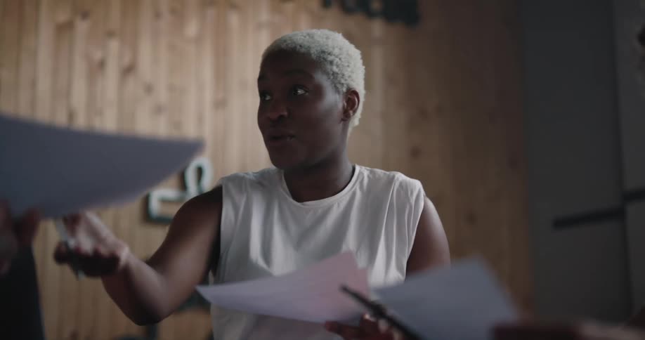 Black woman sitting at the table in an office meeting talking and laughing while collecting papers from the coworkers