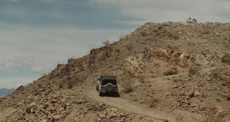 A jeep is climbing a desert mountain road overlooking mountains