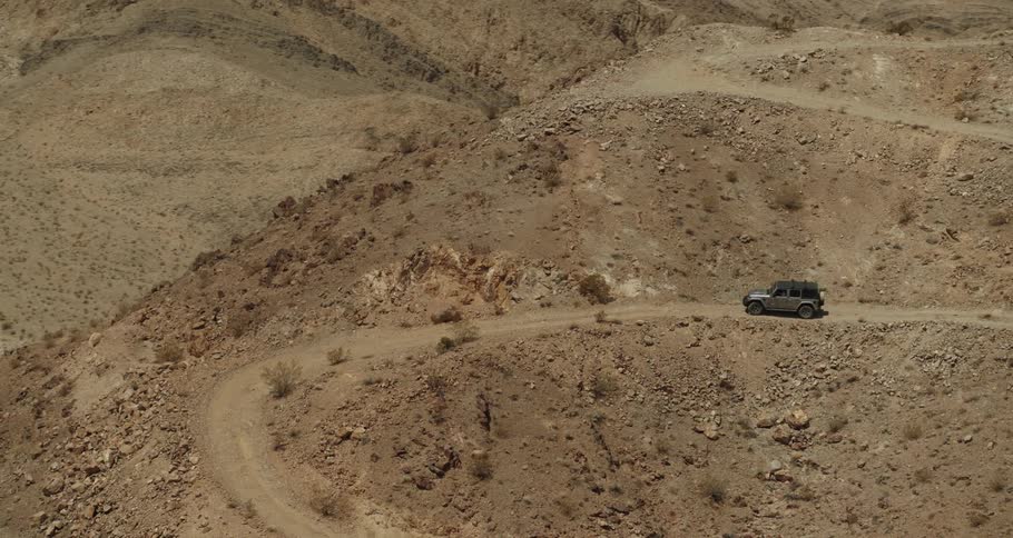 Aerial view of a vehicle driving down a dirt road on a deserted hill near the mountains