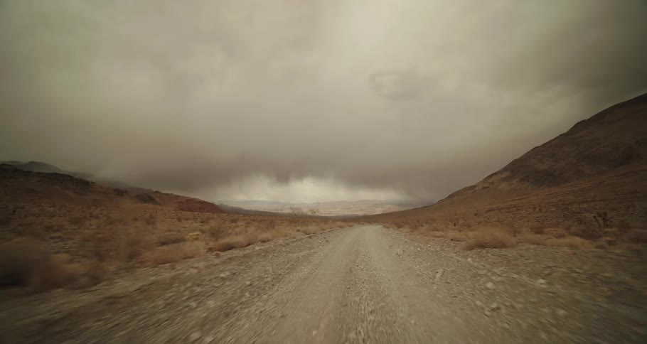 A rocky dirt road passes through a barren stretch of desert under a cloudy sky