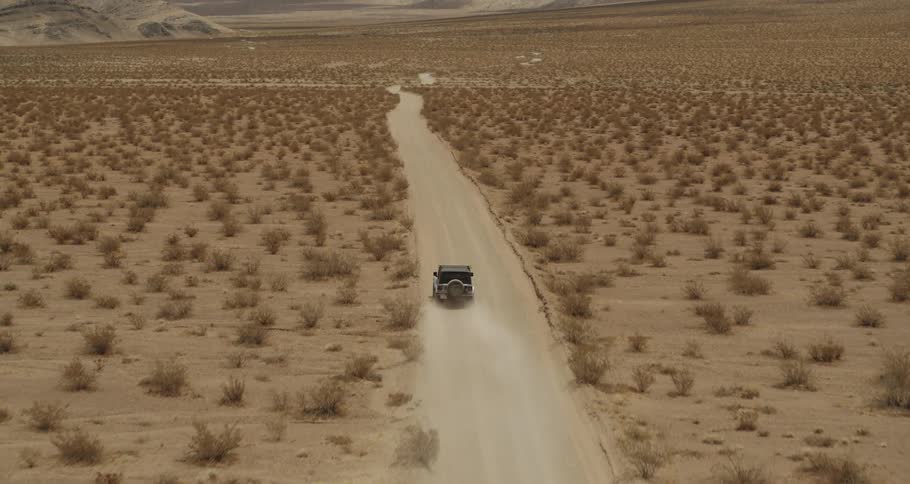 A jeep is traveling on a dirt road through the desert and there are mountains in the distance