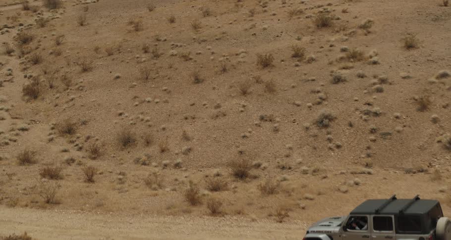 A vehicle travels along a dirt road through the desert during the day