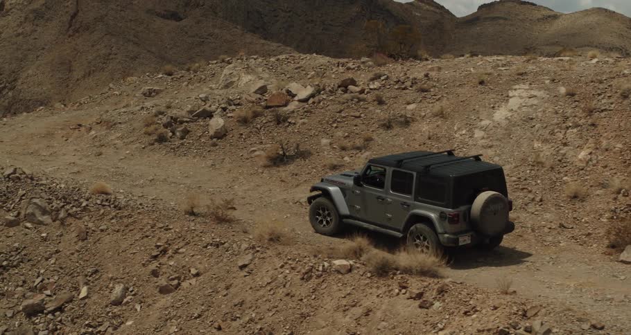 A jeep is traveling on a dirt road in the desert surrounded by mountains