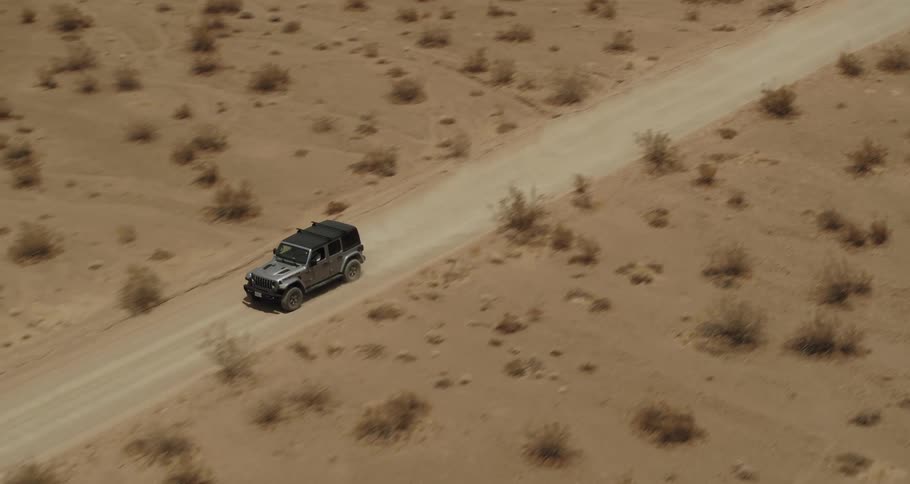 Aerial view of a car driving on a dirt road through the badlands