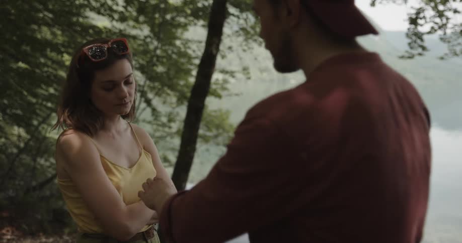 A man and woman stand on the shore and he shows her his cell phone and they fight and she pushes him away