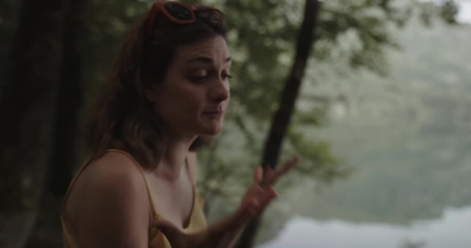 A man approaches a woman standing on the shore of a lake and they begin to argue