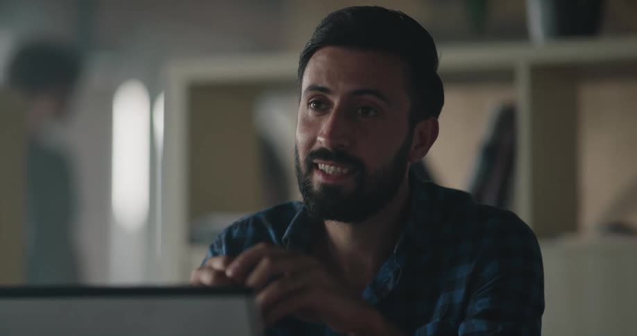 A man laughs during a conversation while sitting at his desk behind a monitor