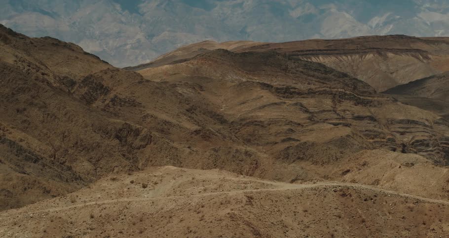 Aerial view of a dirt road atop a hill in the desert close to the mountains