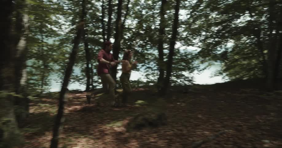 Couple walk along trail through woods arriving at bench overlooking water