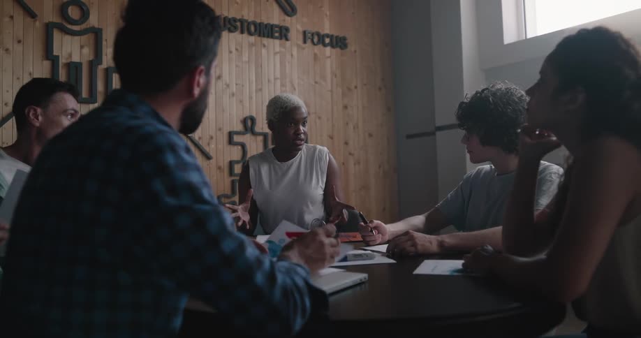 A woman speaks to a group of people sitting with her around a table during a meeting indoors during the day