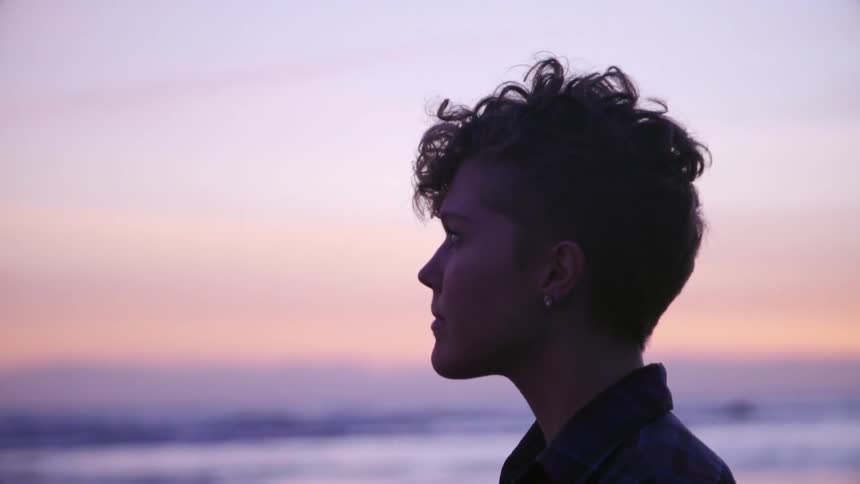A woman is standing on the beach at sunset