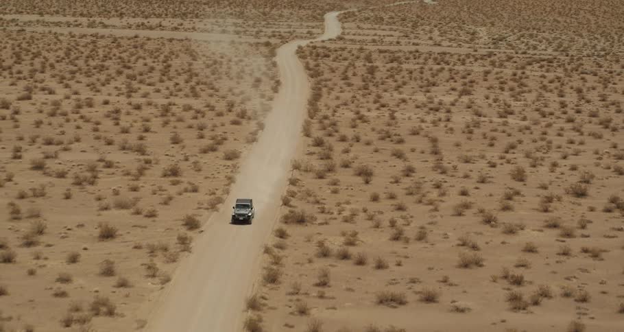 A car is driving through the desert during the daytime