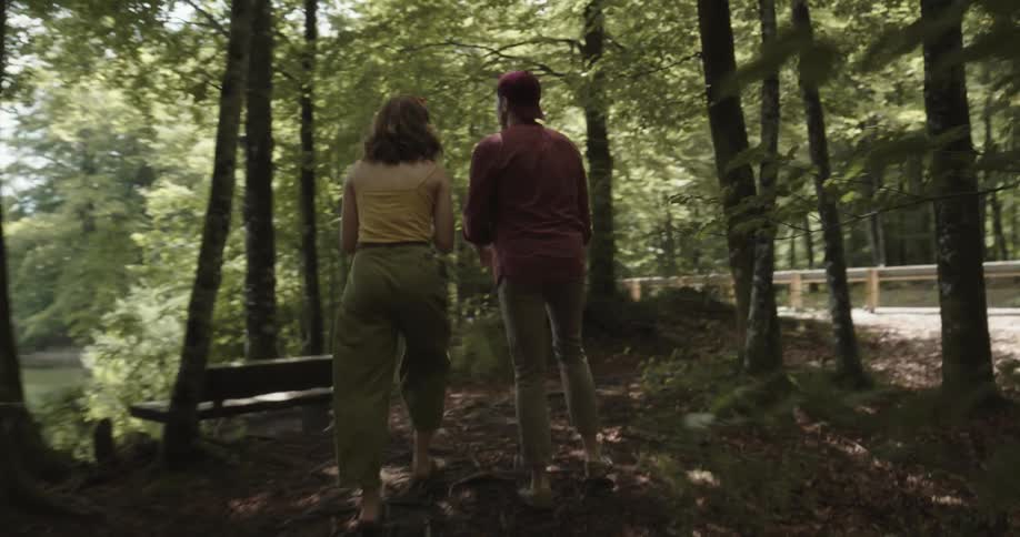 Man runs after a woman in the forest next to a lake and they argue and she angrily grabs a cellphone from his hand