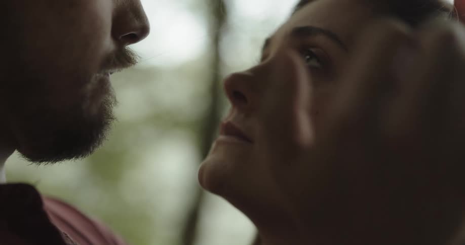 A man caresses the head and face of a woman while embracing her outdoors during the day