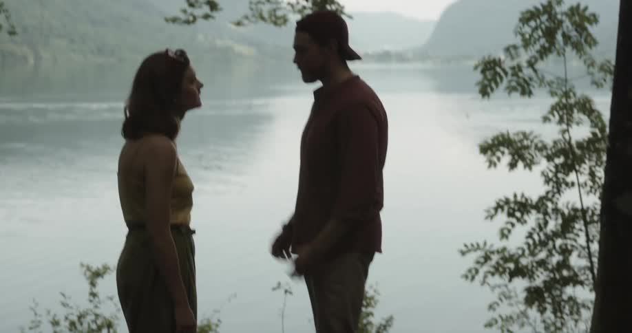 Young couple standing in the forest arguing near a lake in the mountains