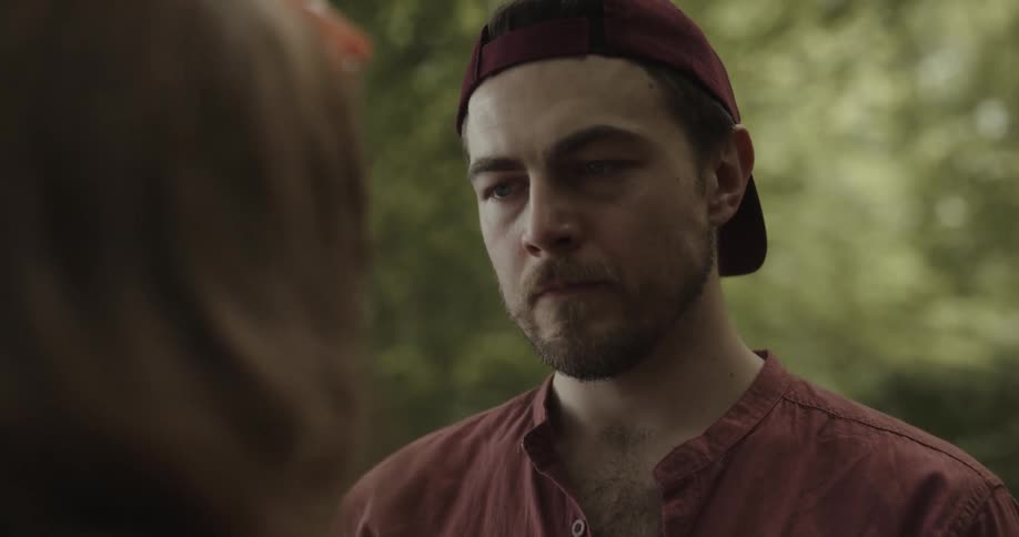 Boyfriend with red cap and shirt approcahes girlfriend and she pushes him away in the woods