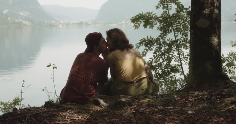 Couple sitting in front of a lake at a sunny day kissing romantically