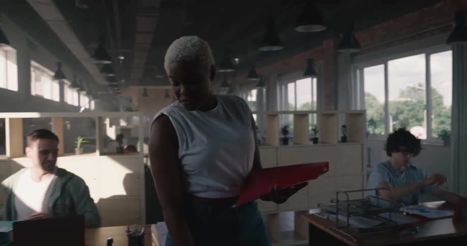 Woman walks through office talking to different employees sitting at their desks