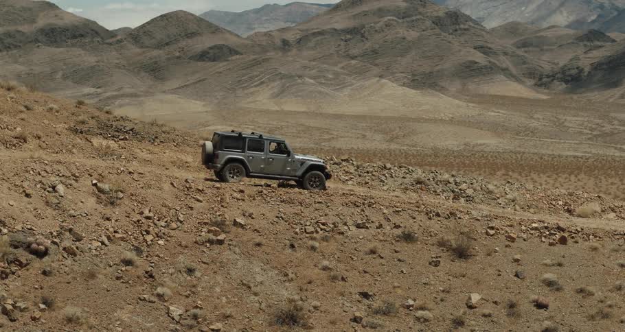 A jeep is traveling on a dirt mountain road in the desert surrounded by more mountains