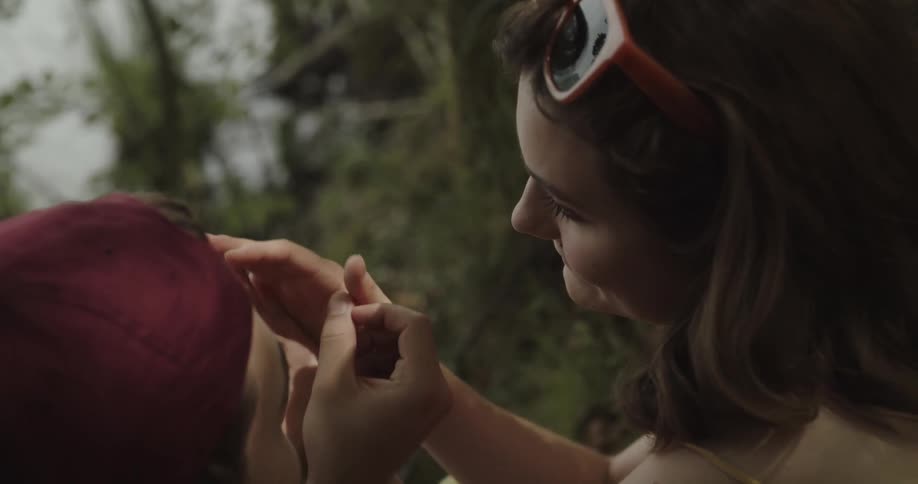 Woman and man touch their hands together romantically as they sit in the forest by the lake