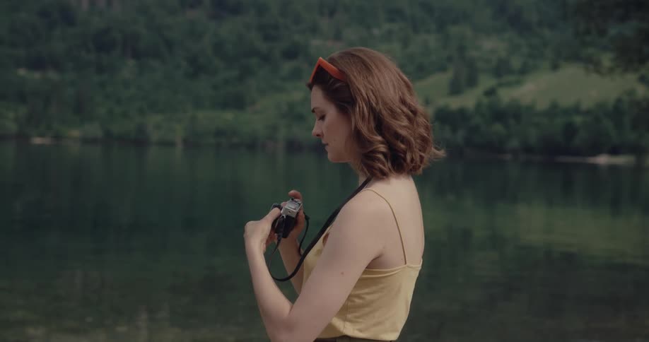 Young woman standing on the shore of a lake in the mountains takes pictures with a vintage roll camera