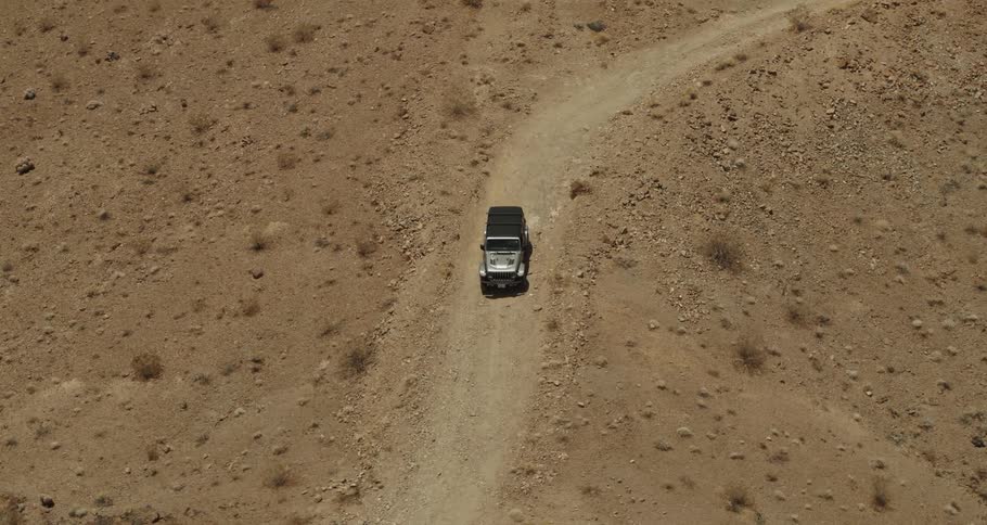 Aerial view of a jeep traveling on a dirt road in the desert