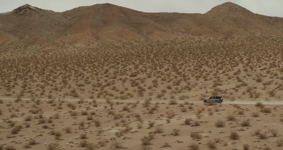A jeep is traveling on a dirt road through the desert with mountains in the distance
